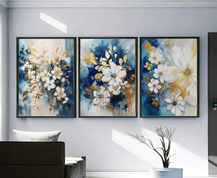 Three floral paintings in blue, white, and gold on a wall in a living room.