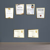 Golden custom diploma frames displaying certificates arranged in a collage on a gray wall above a wooden floor. - Diploma/ Certificate Frames A4 Size - Black / Pack of 2 - Frame World