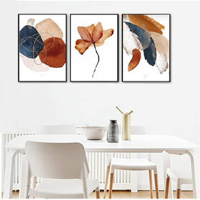 Set of 3 abstract photo frames with brown, navy, and beige tones hanging above a white dining table with chairs.