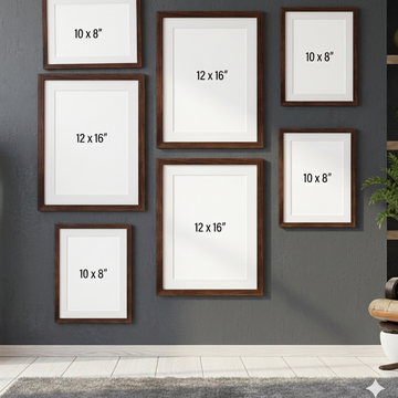 Six wooden picture frames in different sizes mounted on a dark gray wall, each with a white mat and printed size labels such as 10 x 8" and 12 x 16". A small plant and part of a chair are visible at the right edge, and a light floor is below.