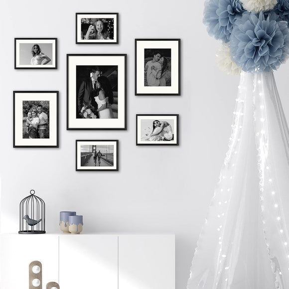 A set of seven picture frames of various sizes arranged in a collage on a wall, featuring glass front panels.