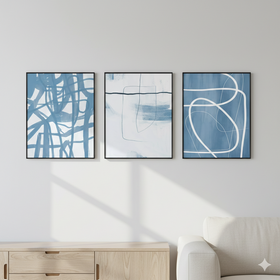 Three abstract art pieces in blue and white frames on a wall above a sofa.