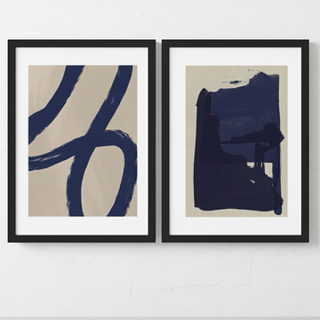 Two abstract artworks with blue brush strokes on beige backgrounds, framed in black, against a white wall.