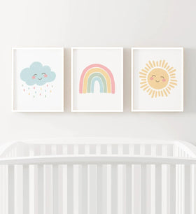 Three colorful prints of a cloud, rainbow, and sun above a crib on a white wall.