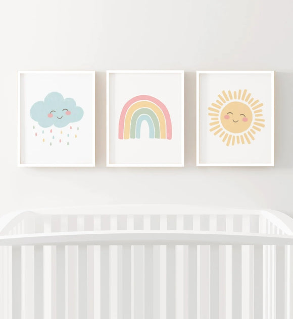 Three colorful prints of a cloud, rainbow, and sun above a crib on a white wall.