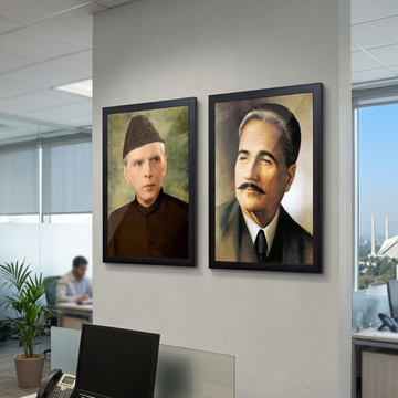 Two framed portrait prints of historical Pakistani leaders,Quaid e azam and Allama iqbal, displayed side-by-side on a light gray office wall above a desk with a computer and phone.
