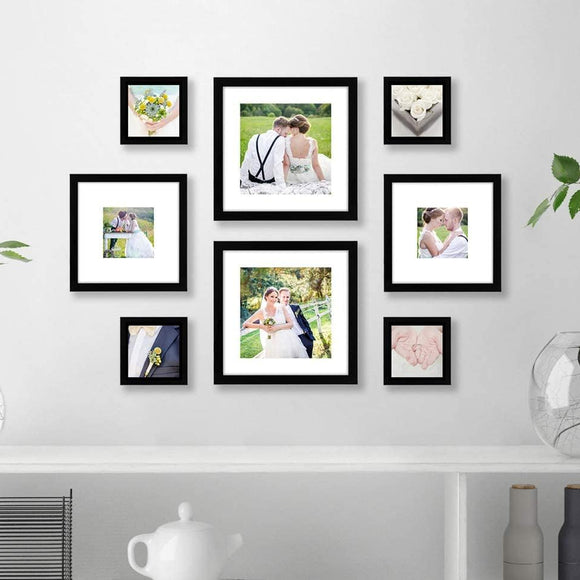 A set of 8 black picture frames of varying sizes arranged in a collage pattern on a white wall above a white shelf with books, a teapot, and decorative items.