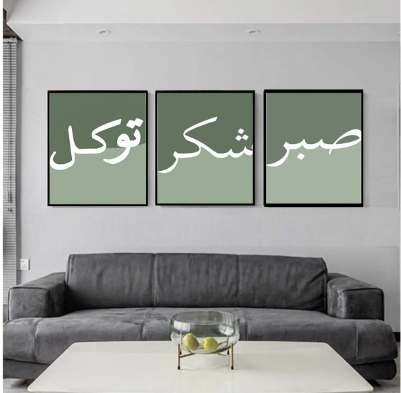 A set of three framed calligraphy art prints in green, hanging on a wall above a grey sofa, with a glass cover on each frame.