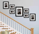 Staircase with wall-mounted black frames containing black and white photos on a light blue wall.