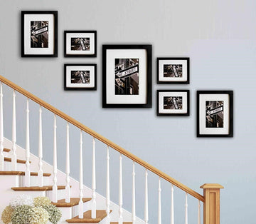 Staircase with wall-mounted black frames containing black and white photos on a light blue wall.