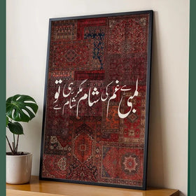 Framed artwork with intricate patterns and Arabic text on a textured background, placed on a wooden surface with a plant.
